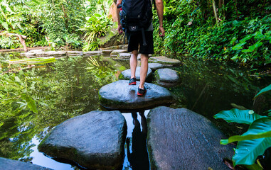 Male hiker with backpack crossing a river on stones