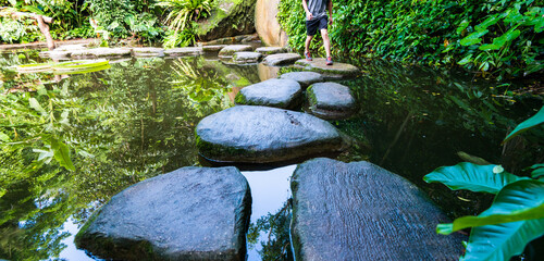 Young man walking crossing a river on stones