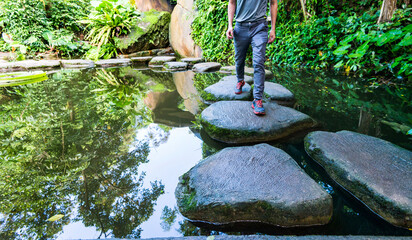 Young man walking crossing a river on stones