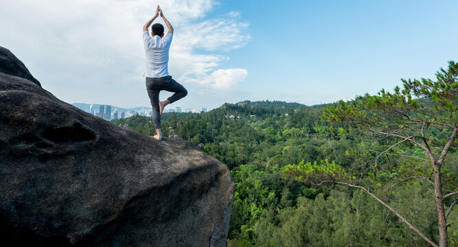 Young man doing yoga on mountain peak - Powered by Adobe