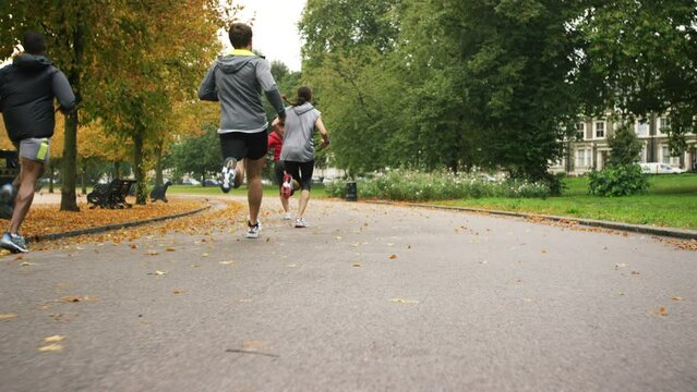 A diverse group of people completing a cardio workout and running through a park together. Back of a group of friends jogging through a garden together. Friends training together running on a park