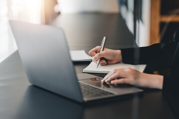Cropped photo of woman writing making list taking notes in notepad working or learning on laptop indoors- educational course or training, seminar, education online concept