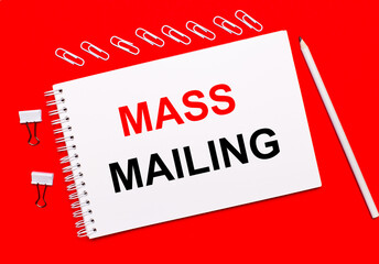 On a bright red background, a white pencil, white paper clips, and a white notebook with the text MASS MAILING