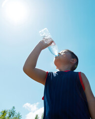 Little asian boy drinking water against blue sky