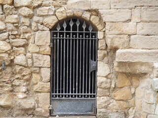Fototapeta na wymiar puerta de acceso a las galerías subterráneas de la iglesia de san juan bautista de vinaixa, arco de piedra y verja de acero color negro, lerida, españa, europa