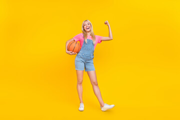 Fototapeta na wymiar Full length photo of positive pretty person hold ball arm show flexing biceps isolated on yellow color background