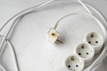 Burnt electric extension cord plug after a short circuit, gray concrete background.