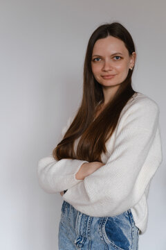 Happy young brunette woman in her 20s over white wall. Employee in casual outfit looking at the camera. Female with long hair, cheerful freelancer business portrait. Copy space