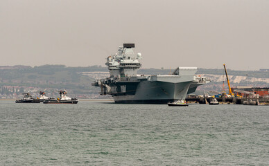 Port Portsmouth, Hampshire, England, UK. 2022. Tugs in attendace to rotate the aircraft carrier HMS Prince Charles in Portsmouth Harbour UK.