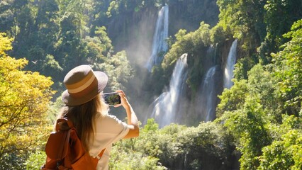 Back view of millennial travel woman on trip or adventure. Young travel blogger on waterfall, make...