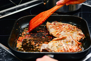 Fried pork steaks in a frying pan. The cook turns the meat for frying.