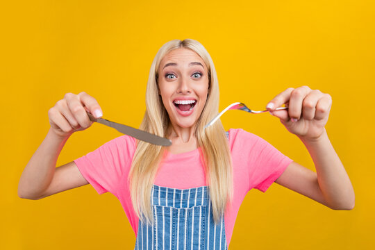 Portrait of attractive cheerful blond girl holding fork knife eating cfresj mealuisine isolated over bright yellow color background