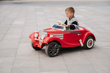 A little boy poses in a mini racing car. Play and relax in the fresh air. - obrazy, fototapety, plakaty