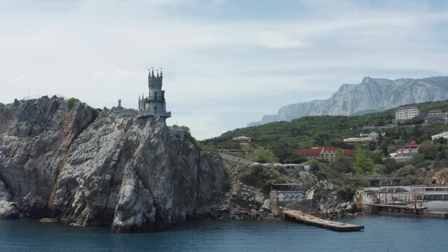 Aerial view of breathtaking rock and Swallow's Nest castle in Crimea, Russia. Action. Touristic place built on the cliff top with green trees and cloudy sky on the background.
