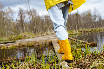 The legs of a woman in yellow boots walk on a wooden platform next to a forest lake