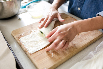 woman preparing spanikopita with phyllo dough on wooden cutting board