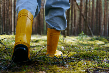 The legs of a woman in yellow boots walk on forest moss