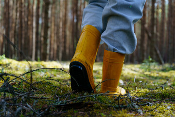 The legs of a woman in yellow boots are walking through the forest