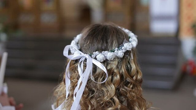 A girl with a wreath on her head stands at the first communion in the church.