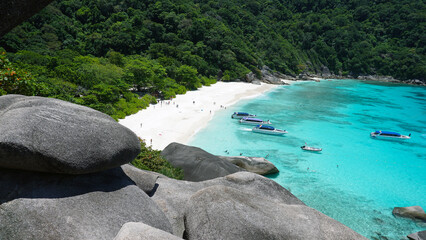 Turquoise water in the bay. View of the island and the sea. High cliffs covered with green trees. The gradient of water from blue to blue. There are speedboats, people swim in places. Similan Islands - Powered by Adobe