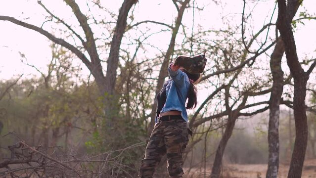 Portrait of happy Indian female holding camera in hand and spreading arms while standing at forest. Woman enjoying nature at Sasan Gir, Junagadh, India. 