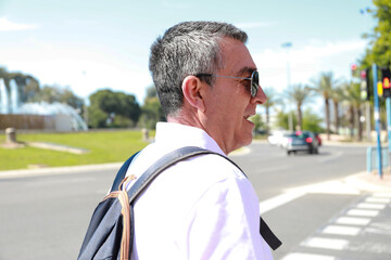 A 60 year old man wearing sunglasses, on summer vacation sightseeing in the city of Alicante walking 