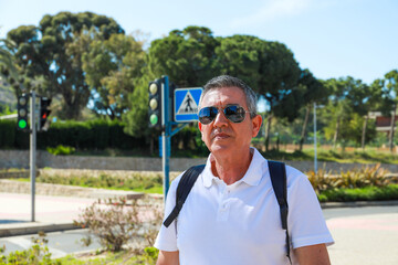 A 60 year old man wearing sunglasses, on summer vacation sightseeing in the city of Alicante walking 
