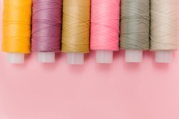 Sewing tools and sewing accessories on elegant pink background. Dressmaking, tailor background. Multicolor sewing threads, thread spools, needles, pins. Top view, flat lay for tailor's business