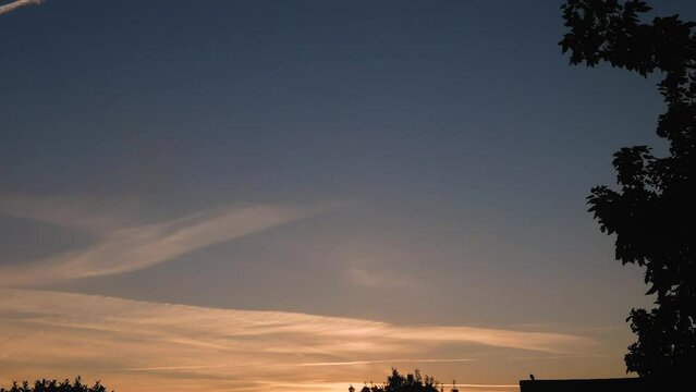 Time lapse of orange and pink cloudy sunset above green trees