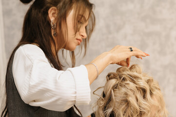 Shooting in a beauty salon. A hair stylist makes a hairstyle for a young dark-haired girl with the help of a hair styler.