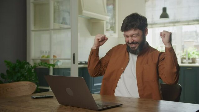 Portrait of a young adult man recieving good news and performing a win dance in front his laptop