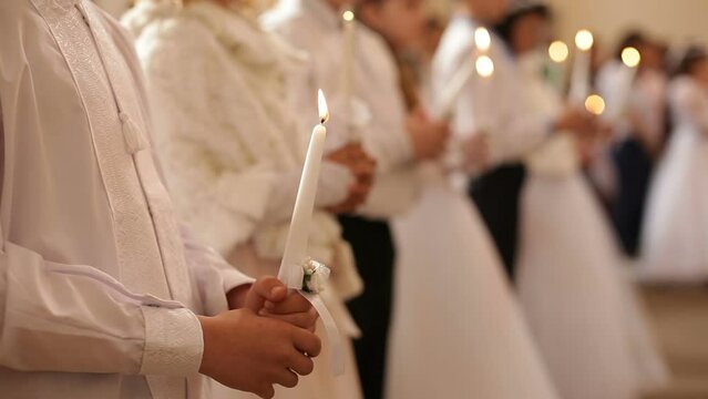 Children stand in the church at the first communion and hold lit candles in their hands. Christian traditions, children receive the Eucharist.