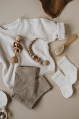 Flatlay aesthetic Scandinavian newborn baby clothes, care accessories, toys on neutral pastel beige colour background. Trendy elegant luxury infant set. Top view