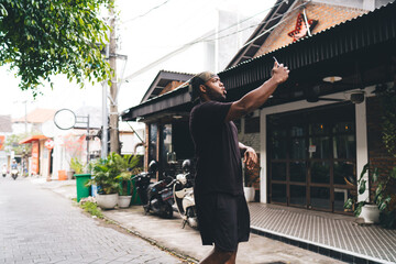 African American tourist in bandanna clicking selfie images during free time in city, emotional hipster guy using smartphone front camera for shooting influence video about traveling lifestyle