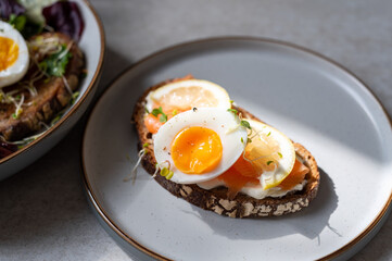 Healthy breakfast or snack with medium boiled eggs on toasted bread with cheese cream, salmon and lemon slices on grey plate