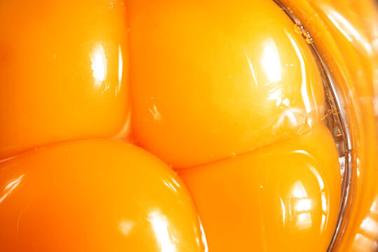 Close-up of egg yolks. Broken eggs and yolks next to each other. Smooth and moist surface with reflections.