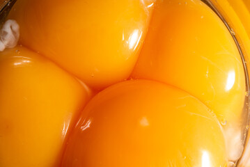 Close-up of egg yolks. Broken eggs and yolks next to each other. Smooth and moist surface with reflections.