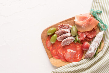 Variety of meat snacks, charcuterie plate with different types of sausages - salami, bresaola, proscuitto served with olives, rosematy and fresh grape. Wooden cutting board with italian antipasti