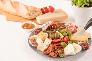 Antipasti plate with variety of cheeses, sausages served with sun dried tomatoes, olives, jams and herbs on white table - parmesan, dorblu, prosciutto, salami. Cheese and meat snacks platter