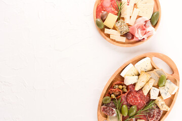 Wooden plates with traditional Italian antipasti - variety of cheeses, sausages served with sun dried tomatoes, olives  and herbs on white table - parmesan, dorblu, prosciutto, salami
