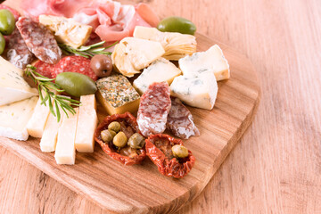 Italian antipasti, wooden cutting board with variety of cheeses, sausages served with sun dried tomatoes, olives and herbs on wooden table. Cheese and meat snacks platter