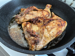 Two chicken legs are fried in a pan in a large amount of oil.