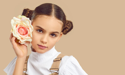 Closeup fashion shot of beautiful teen girl isolated on nude brown studio background pose with rose. Pretty teenager child model with flower. Children photography. Copy space, advertising.