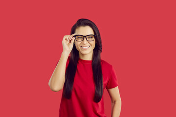 Portrait of smiling young woman wearing glasses need sight correction for better vision. Happy female client in spectacles after optician appointment. Eyewear prescription. Red studio background.