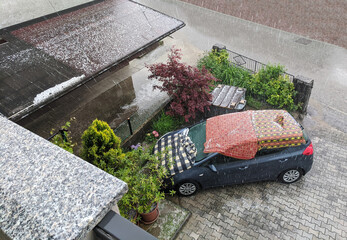Car covered in blankets during strong hail storm. Car protection against hail during stormy weather - obrazy, fototapety, plakaty