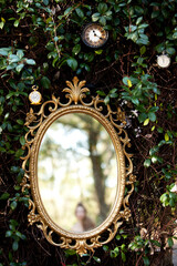 Alice in Wonderland Gold Mirror Outdoors in Garden with vines and Clocks with Girl's Reflection in Mirror