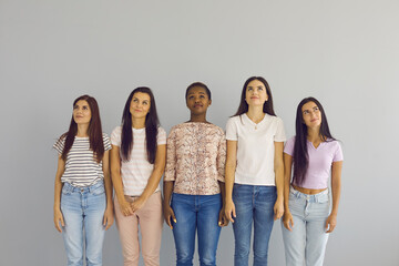 Happy millennial gen z multiethnic girls on grey wall background look up thinking making choice decision. Pensive smiling young multiracial diverse women consider good sale deal. Copy space.