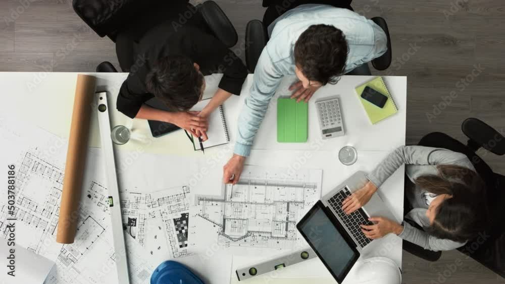 Aufkleber A group of architects calculating their finances using a building blueprint from above. A group of businesspeople talking about blueprints when brainstorming in a meeting using a laptop and calculator