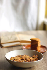 Bowl of chocolate chip cookies, plate of biscuits, open books and reading glasses on the table. Selective focus.