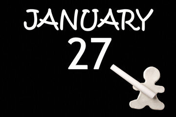 A small white plasticine man writing the date 27 January on a black board. Business concept. Education concept.